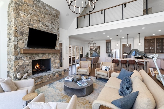 living room featuring a high ceiling, an inviting chandelier, a stone fireplace, crown molding, and hardwood / wood-style floors