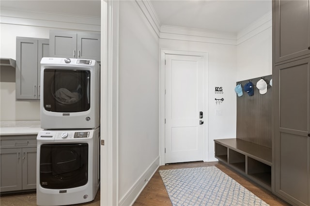 clothes washing area with dark wood-type flooring, cabinets, stacked washer and clothes dryer, and ornamental molding