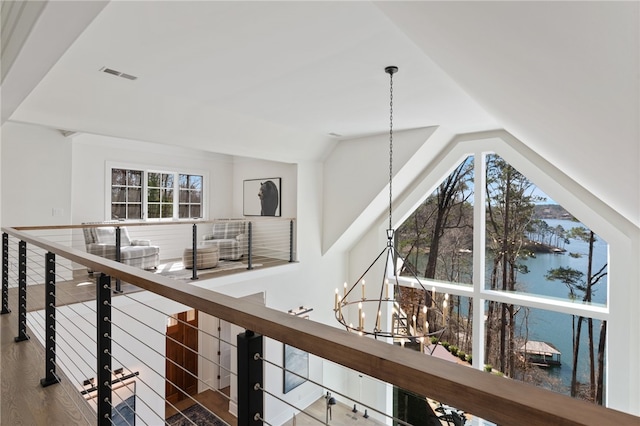 hallway with hardwood / wood-style floors, an inviting chandelier, a water view, and vaulted ceiling