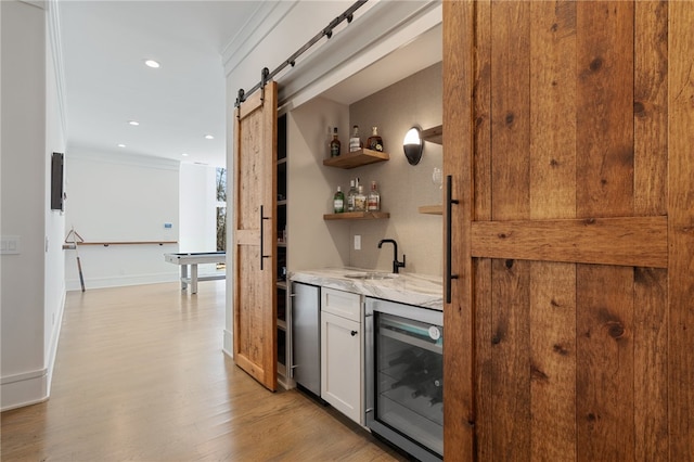 bar featuring beverage cooler, crown molding, sink, a barn door, and white cabinetry