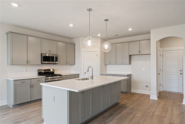 kitchen with stainless steel appliances, an island with sink, sink, and gray cabinets