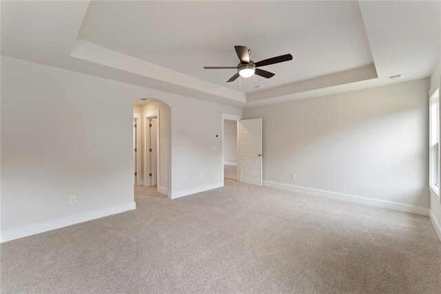 carpeted empty room featuring ceiling fan and a raised ceiling