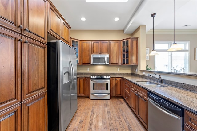 kitchen with sink, appliances with stainless steel finishes, dark stone countertops, crown molding, and light hardwood / wood-style floors