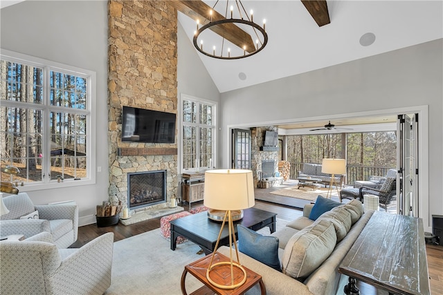 living room featuring high vaulted ceiling, ceiling fan with notable chandelier, a stone fireplace, beamed ceiling, and hardwood / wood-style floors