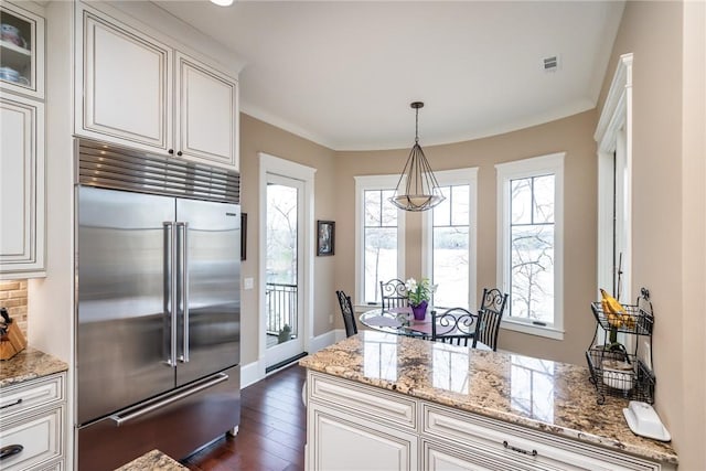 kitchen featuring pendant lighting, glass insert cabinets, stainless steel built in fridge, white cabinetry, and light stone countertops