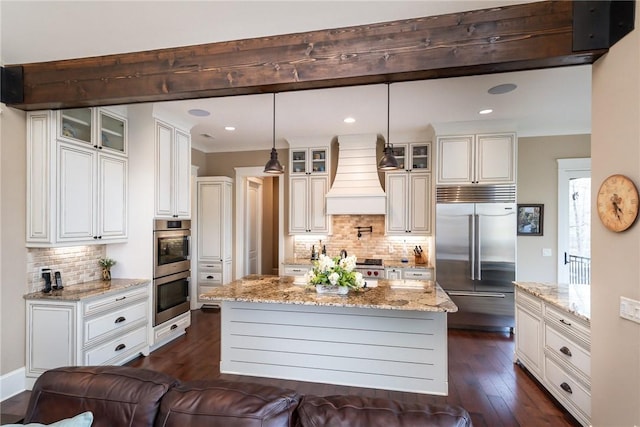 kitchen with custom exhaust hood, glass insert cabinets, stainless steel appliances, and a center island