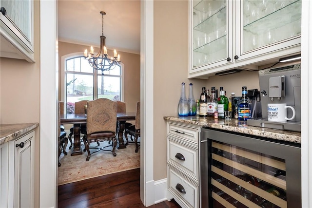 bar with beverage cooler, dark wood-style flooring, decorative light fixtures, a bar, and a notable chandelier