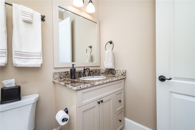 half bathroom featuring toilet, baseboards, and vanity