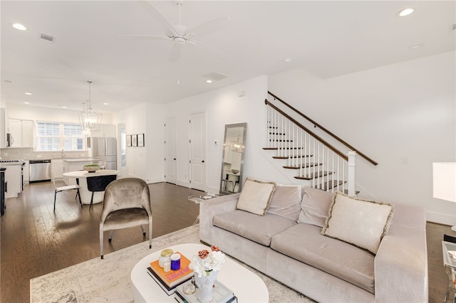 living room featuring ceiling fan with notable chandelier and dark wood-type flooring