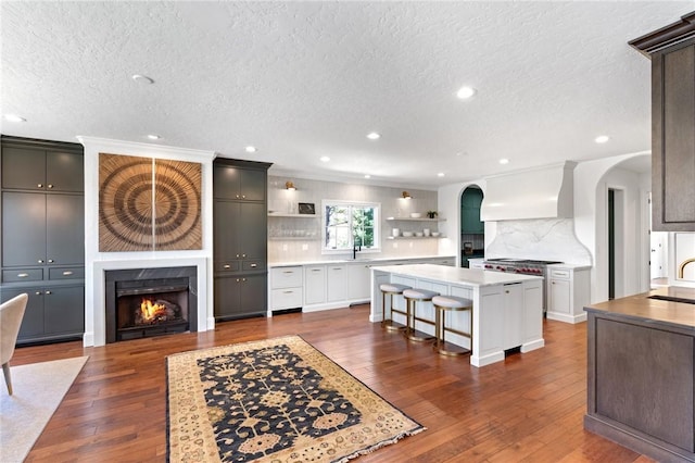 kitchen with custom exhaust hood, dark wood-type flooring, tasteful backsplash, a kitchen island, and a kitchen bar