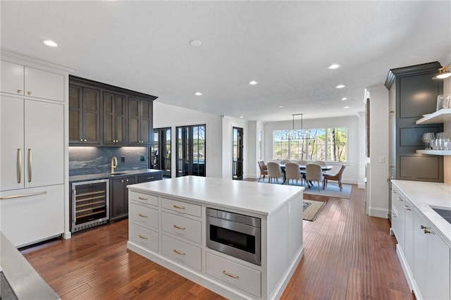 kitchen featuring built in microwave, a center island, beverage cooler, decorative light fixtures, and decorative backsplash