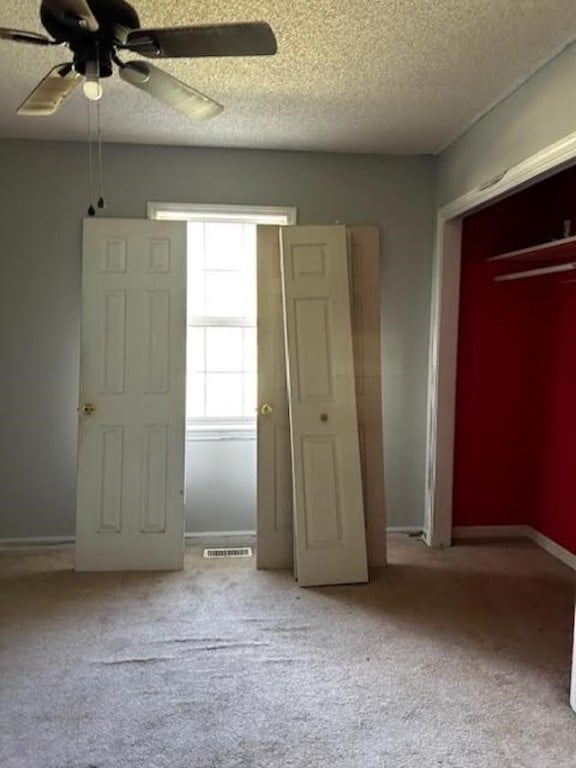 unfurnished bedroom with a textured ceiling, ceiling fan, and light colored carpet