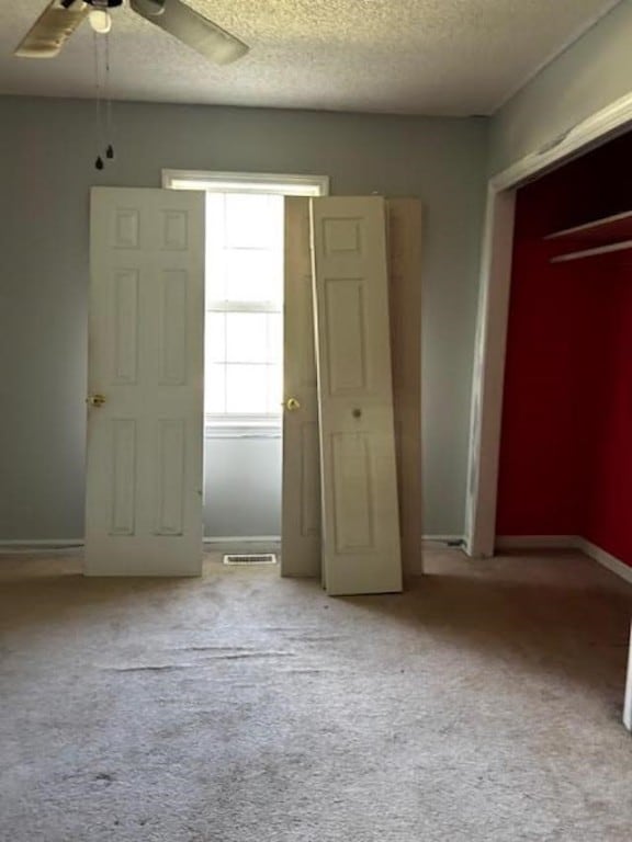 unfurnished bedroom featuring ceiling fan, light colored carpet, and a textured ceiling