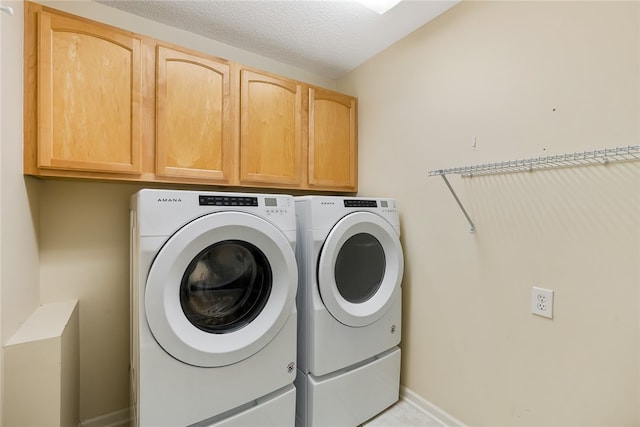 laundry area featuring washer and dryer, a textured ceiling, and cabinets