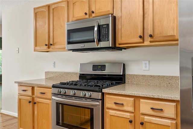 kitchen with light brown cabinetry, appliances with stainless steel finishes, light stone counters, and light wood-type flooring