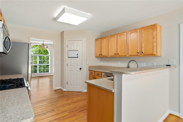 kitchen featuring kitchen peninsula, a textured ceiling, stainless steel appliances, and light wood-type flooring