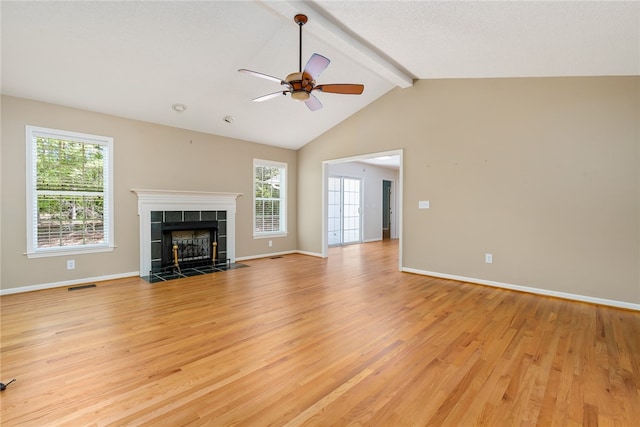 unfurnished living room featuring a tiled fireplace, lofted ceiling with beams, light hardwood / wood-style flooring, and ceiling fan