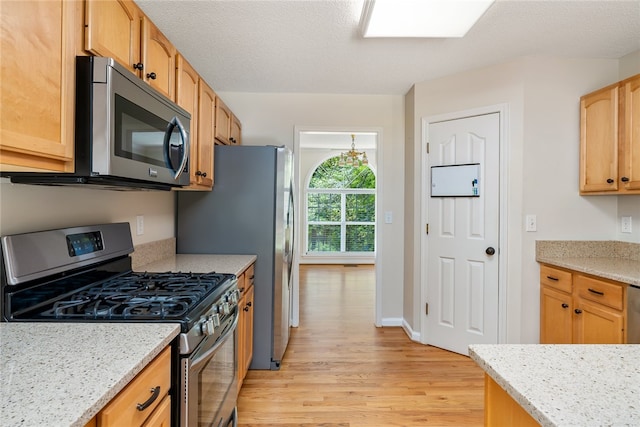 kitchen featuring light stone countertops, appliances with stainless steel finishes, a textured ceiling, and light hardwood / wood-style floors