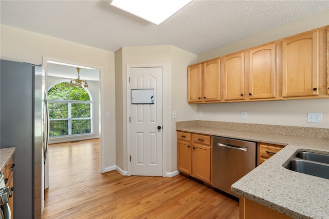 kitchen with light brown cabinets, stainless steel appliances, light stone counters, a textured ceiling, and light hardwood / wood-style floors