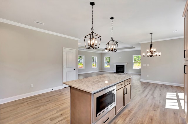 kitchen featuring ornamental molding, decorative light fixtures, stainless steel microwave, and light hardwood / wood-style floors