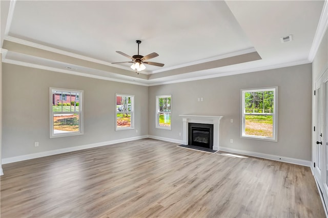 unfurnished living room featuring a raised ceiling, crown molding, light hardwood / wood-style flooring, and a wealth of natural light