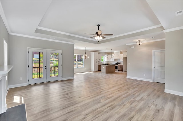 unfurnished living room with ceiling fan with notable chandelier, a raised ceiling, crown molding, light hardwood / wood-style flooring, and french doors