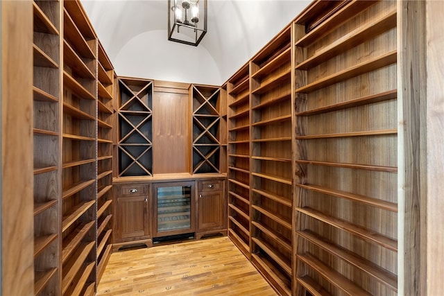 wine cellar with an inviting chandelier, light hardwood / wood-style flooring, wine cooler, and vaulted ceiling