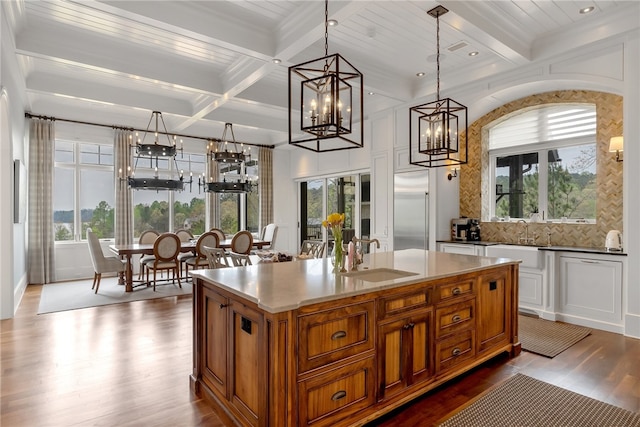 kitchen with beamed ceiling, light hardwood / wood-style flooring, a center island with sink, sink, and decorative light fixtures