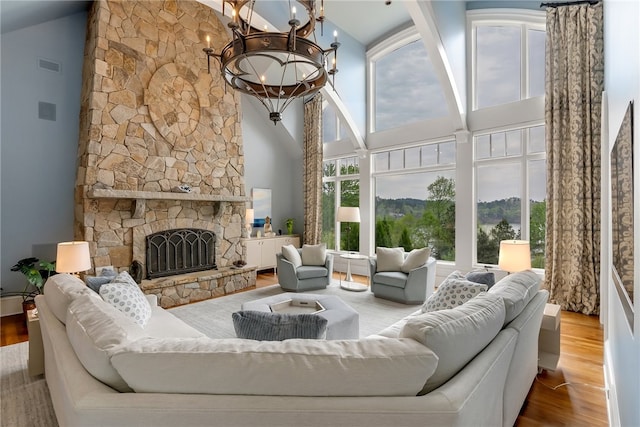 living room with high vaulted ceiling, light hardwood / wood-style flooring, a fireplace, and an inviting chandelier