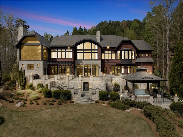 back house at dusk featuring a patio, a gazebo, a lawn, and a balcony