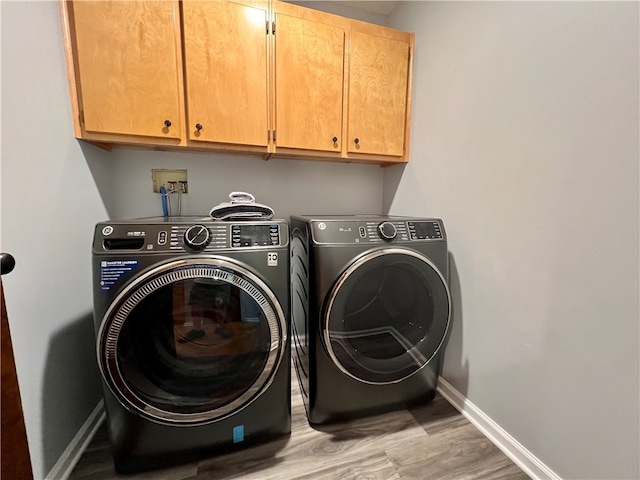 clothes washing area with cabinets, light wood-type flooring, and independent washer and dryer