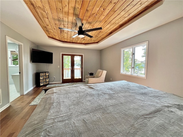 bedroom featuring ceiling fan, hardwood / wood-style flooring, a tray ceiling, and multiple windows