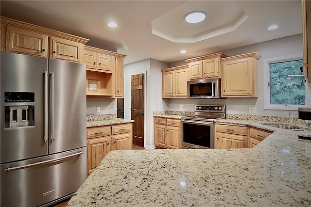 kitchen featuring light stone countertops, stainless steel appliances, a tray ceiling, and light brown cabinets