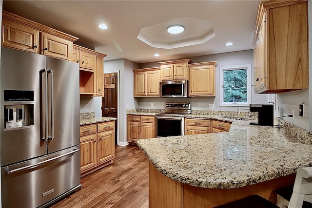 kitchen with appliances with stainless steel finishes, kitchen peninsula, a breakfast bar area, light wood-type flooring, and sink