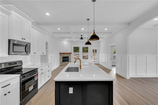 kitchen featuring light hardwood / wood-style flooring, decorative light fixtures, gas stove, a kitchen island with sink, and sink