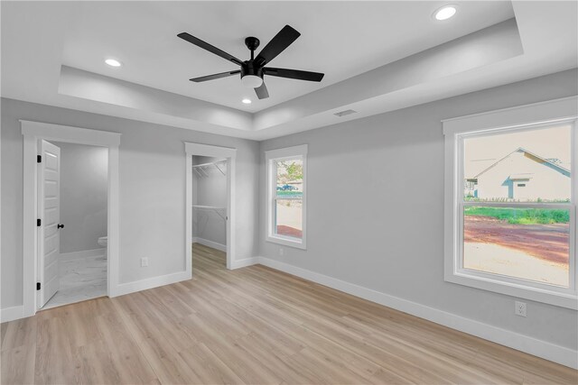 unfurnished bedroom with light hardwood / wood-style flooring, a tray ceiling, ceiling fan, and a spacious closet