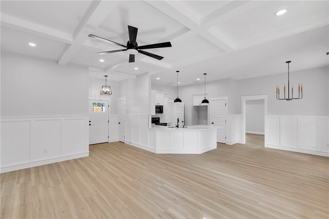 unfurnished living room featuring ceiling fan with notable chandelier, beamed ceiling, coffered ceiling, and light hardwood / wood-style flooring