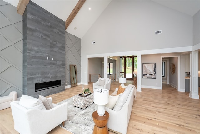 living room with high vaulted ceiling, a tiled fireplace, light hardwood / wood-style floors, and beamed ceiling