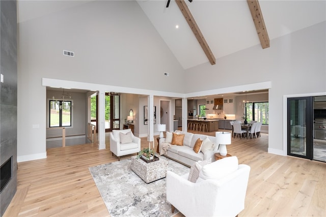 living room featuring beamed ceiling, high vaulted ceiling, a notable chandelier, a fireplace, and light hardwood / wood-style floors