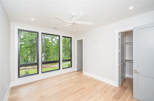 unfurnished bedroom featuring ceiling fan, light hardwood / wood-style flooring, a closet, and a walk in closet