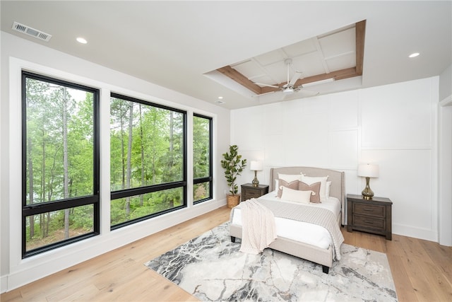 bedroom featuring multiple windows, a raised ceiling, light hardwood / wood-style floors, and ceiling fan