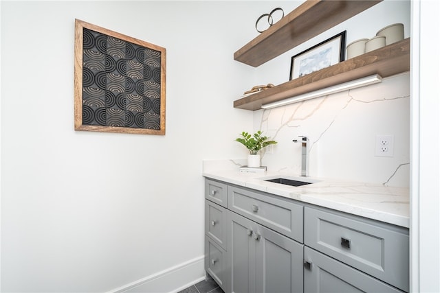 bar featuring dark tile patterned flooring, light stone counters, tasteful backsplash, gray cabinets, and sink