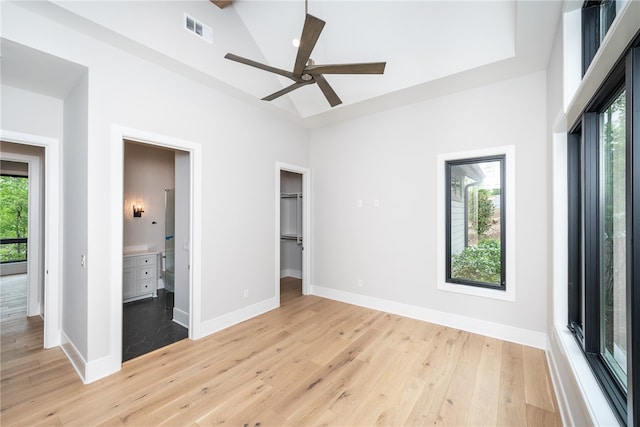 unfurnished bedroom with multiple windows, ensuite bath, ceiling fan, and light hardwood / wood-style flooring