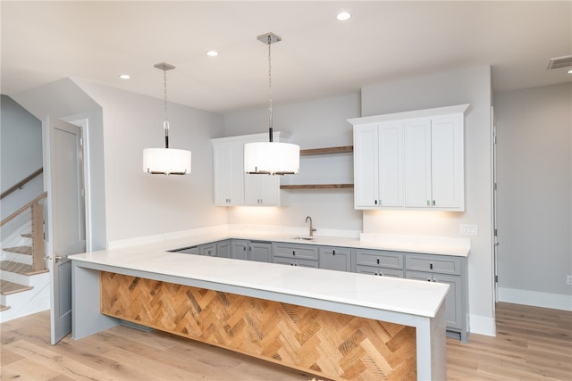 kitchen featuring kitchen peninsula, decorative light fixtures, light hardwood / wood-style flooring, white cabinetry, and gray cabinets