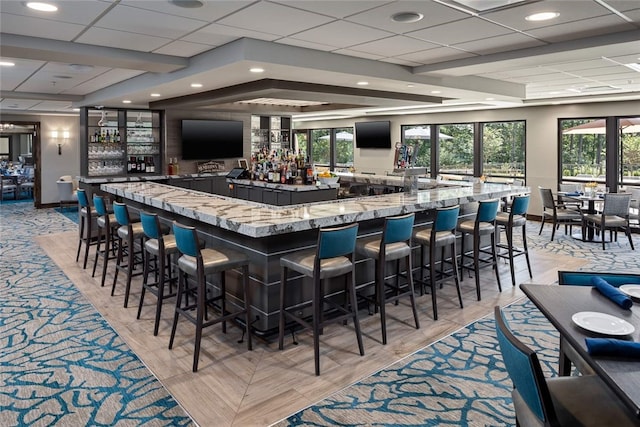 bar featuring plenty of natural light, light hardwood / wood-style floors, light stone counters, and a drop ceiling