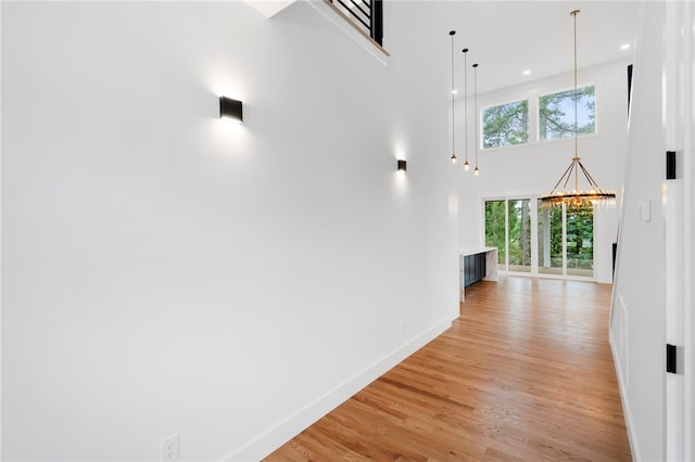 corridor with an inviting chandelier, light hardwood / wood-style floors, and a high ceiling