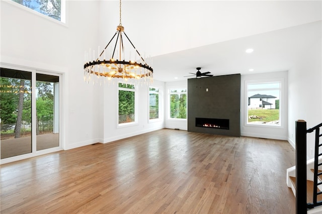 unfurnished living room with wood-type flooring, a fireplace, ceiling fan with notable chandelier, and a wealth of natural light