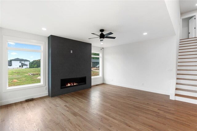 unfurnished living room featuring a wealth of natural light, wood-type flooring, a large fireplace, and ceiling fan