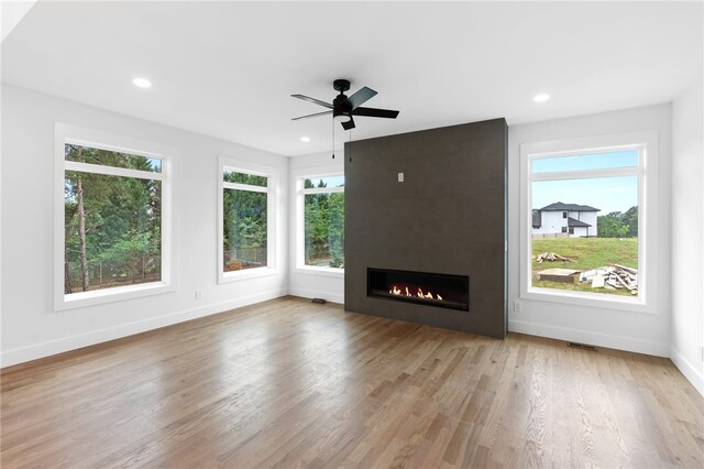 unfurnished living room with a wealth of natural light, light hardwood / wood-style floors, a large fireplace, and ceiling fan