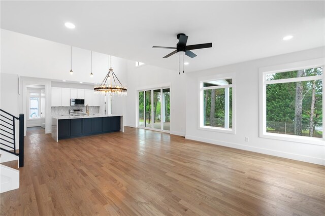 unfurnished living room featuring ceiling fan with notable chandelier, light hardwood / wood-style flooring, and a wealth of natural light